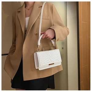Detail of white quilted crossbody bag featuring wave texture and gold metal accents
