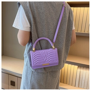 Close-up of a purple quilted small square bag with golden lock and braided handle detail