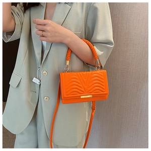 Detail of bright orange wave quilted handbag with leather texture and gold hardware