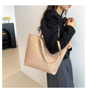 Detail of beige quilted tote bag with metallic rivets and long handles worn by model