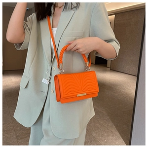 Detail of bright orange quilted leather bag with woven handle and metallic lock closure