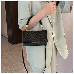 Detail of black quilted crossbody bag with gold hardware and woven handle on a model