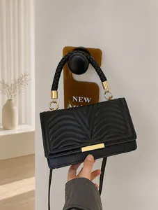 Macro detail of black quilted leather crossbody bag with V-shaped texture and gold buckles