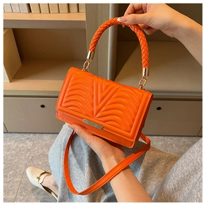 Detail of orange quilted crossbody bag with woven top handle and gold metal trim