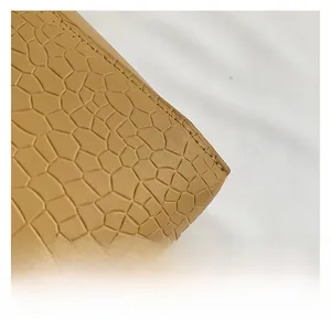 Macro detail of brown crocodile embossed leather with precise stitching on a shoulder bag