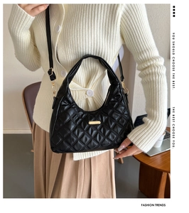 Detail of black quilted shoulder bag with gold hardware held by a woman in office setting