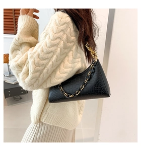 Detail of black crocodile texture shoulder bag featuring chunky gold chain strap on model