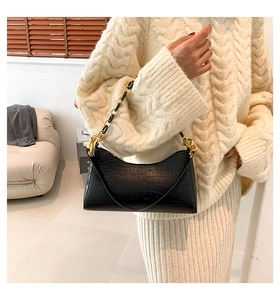 Detail of black crocodile texture leather with gold chain strap on an underarm bag
