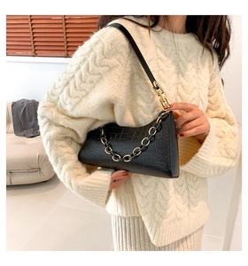 Detail of black crocodile pattern underarm bag with gold chain and white sweater contrast