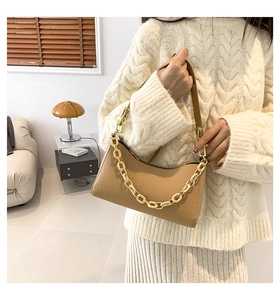 Detail of camel crocodile pattern underarm bag with cream and gold chain on beige knitwear