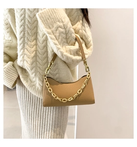 Close-up of brown croc-embossed shoulder bag with chunky gold chain detail on a model
