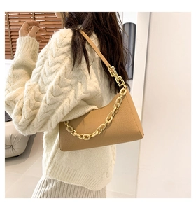 Detail view of beige crocodile embossed underarm bag with decorative gold chain strap