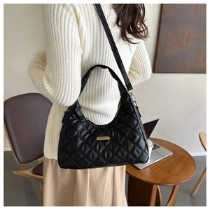 Detail of black quilted shoulder bag with gold zipper and metal plate in cafe setting