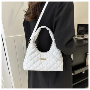 Detail of white quilted handbag with gold logo plate worn by model in black suit