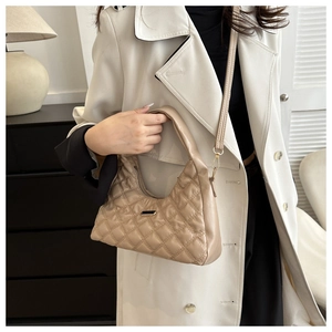 Close-up of quilted diamond pattern and metallic logo on beige shoulder bag worn by model