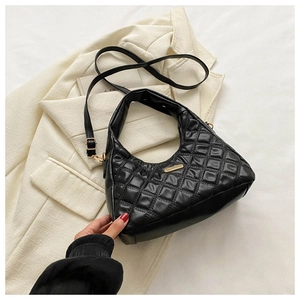 Detail of black quilted shoulder bag with gold hardware on a beige blazer background