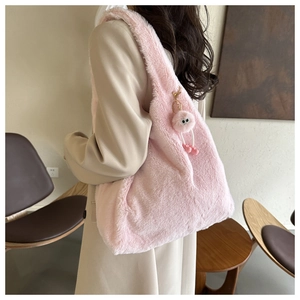 Détail d'un sac seau en peluche rose avec pompon sur l'épaule d'un mannequin