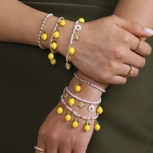 Pearl bracelets with lemon and bee charms displayed on a model's wrist against dark fabric
