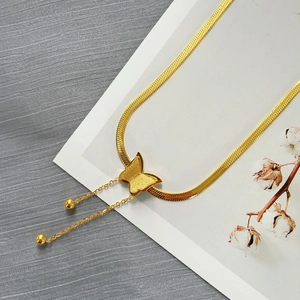 Collana con ciondolo a farfalla dorata con catena a serpente e perline su sfondo materico