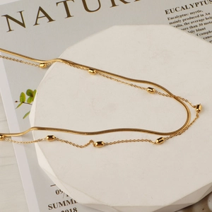 Double-layered titanium steel necklace with gold beads and snake chain on a white display