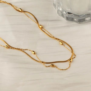 Double-layered gold titanium steel necklace with flat snake chain and small beads on white fabric