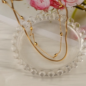 Double-layered gold titanium steel necklace with elegant beads on a glass tray