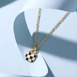 Gold chain necklace with a black and white checkerboard mini bag pendant on blue background