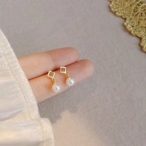 Golden geometric hollow square earrings with pearl pendants worn on fingers