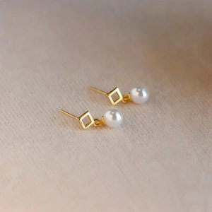 Geometric diamond-shaped gold earrings with white pearls on a light wood background