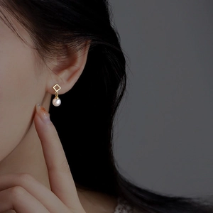 Elegant geometric gold diamond frame pearl stud earrings for women shown on a model