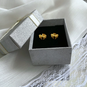 Golden bow stud earrings with brushed texture in a glitter jewelry box on lace background