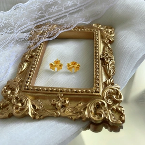 Detailed view of gold bow earrings with matte finish on elegant lace background