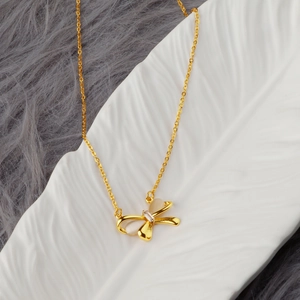 Collana con fiocco dorato, zircone rettangolare e madreperla su un piatto bianco