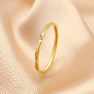 Faceted gold minimalist titanium steel ring with a small diamond on silk background