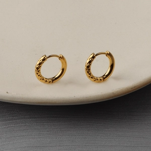 Orecchini a cerchio dorati martellati minimalisti su un piatto di ceramica