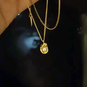 Elegant gold titanium necklace with peanut pearl pendant shown in hand on dark background