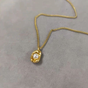 Elegant gold pearl necklace with irregular textured pendant on a dark minimalist background