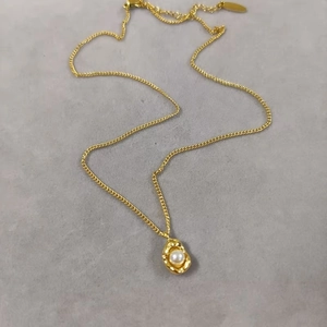 Lava style gold peanut necklace with white pearl pendant on a minimal grey surface