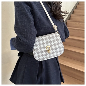 Detailed view of women's houndstooth saddle bag with golden horseshoe buckle and white strap