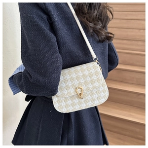 Detail of tweed saddle bag with golden water-drop clasp on navy jacket