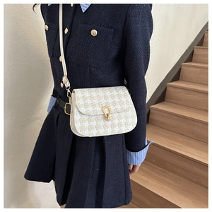 Detail of tweed checkered saddle bag with golden horseshoe buckle and cream leather strap