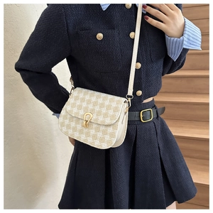 Detail of a plaid tweed saddle bag featuring a gold shield clasp on a navy tweed outfit