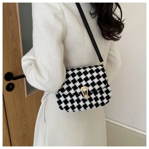Detail of houndstooth plaid crossbody bag with gold U-buckle and black leather strap