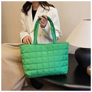 Detailed view of large green quilted puffer tote bag held by a model in a cozy indoor setting