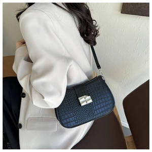 Schwarze Schultertasche mit Krokoprägung und silberner Schnalle auf weißem Blazer