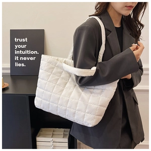 Detailed side view of a white quilted puffer tote bag worn by a model in a cozy room