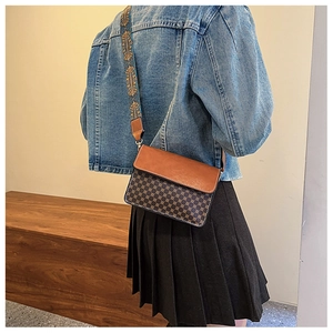 Retro crossbody bag detail featuring wide blue floral strap and brown checkered leather