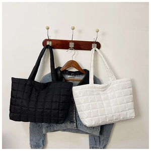 Detailed view of quilted puffer tote bags in black and white colors hanging on a wooden hook