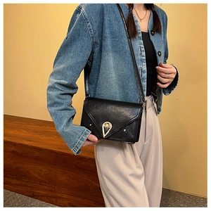 Chic black crossbody bag with gold teardrop lock on a model wearing denim jacket