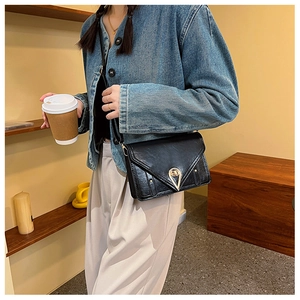Detail of black patent leather crossbody bag with golden teardrop lock and V-flap design